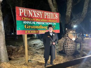 the President of the Ground Hog Club stands in front of a Punxy Phil sign