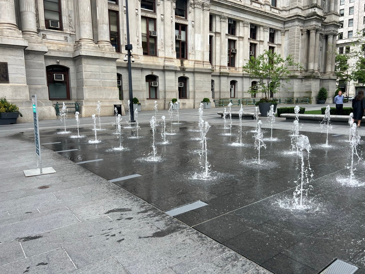 Water sprays from the ground in multiple areas with Philadelphia's City Hall in the background. Dilworth Park hosts one of 90 public Philadelphia Spraygrounds for Philadelphians to cool off in this summer.