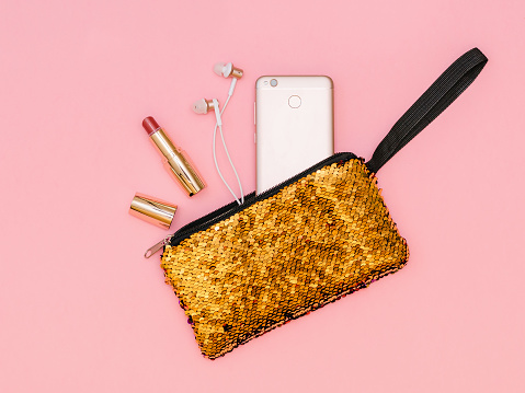 Open lipstick, headphones and phone in a gold-colored bag. Pastel color. Flat lay.