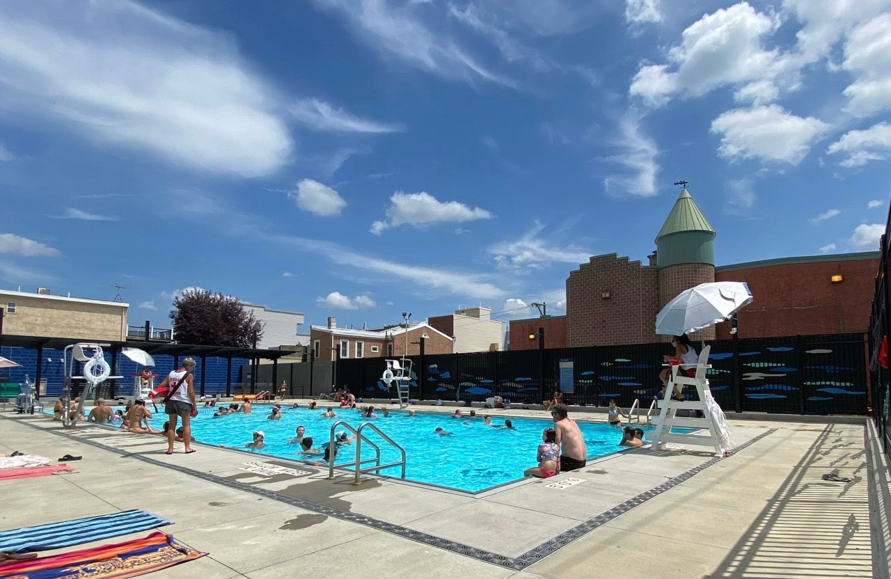 Photo shows a sunny pool day with blue skies and white clouds overhead. You can see at least 3 lifeguards posted around a semi-crowded teal blue pool. It's Fishtown's Lederer Pool, which opens today, Tuesday, June 18th.