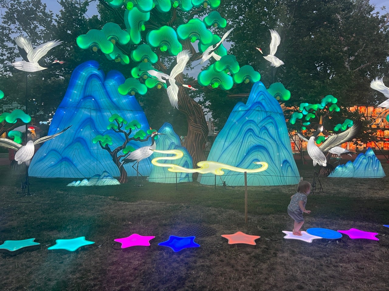 Light up rainbow colored stars stepping stones in all different colors, lined front of beautiful lanterns with colorful blue mountains, green trees and white birds.