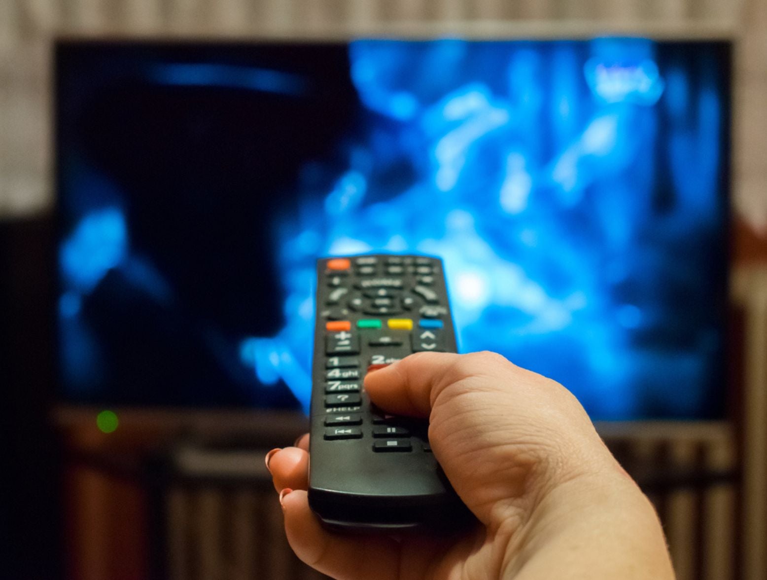 hand on remote pointed at TV